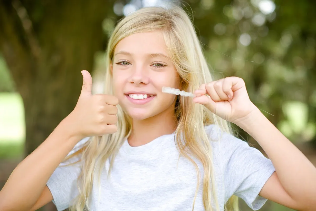 Child holding a clear aligner tray and smiling