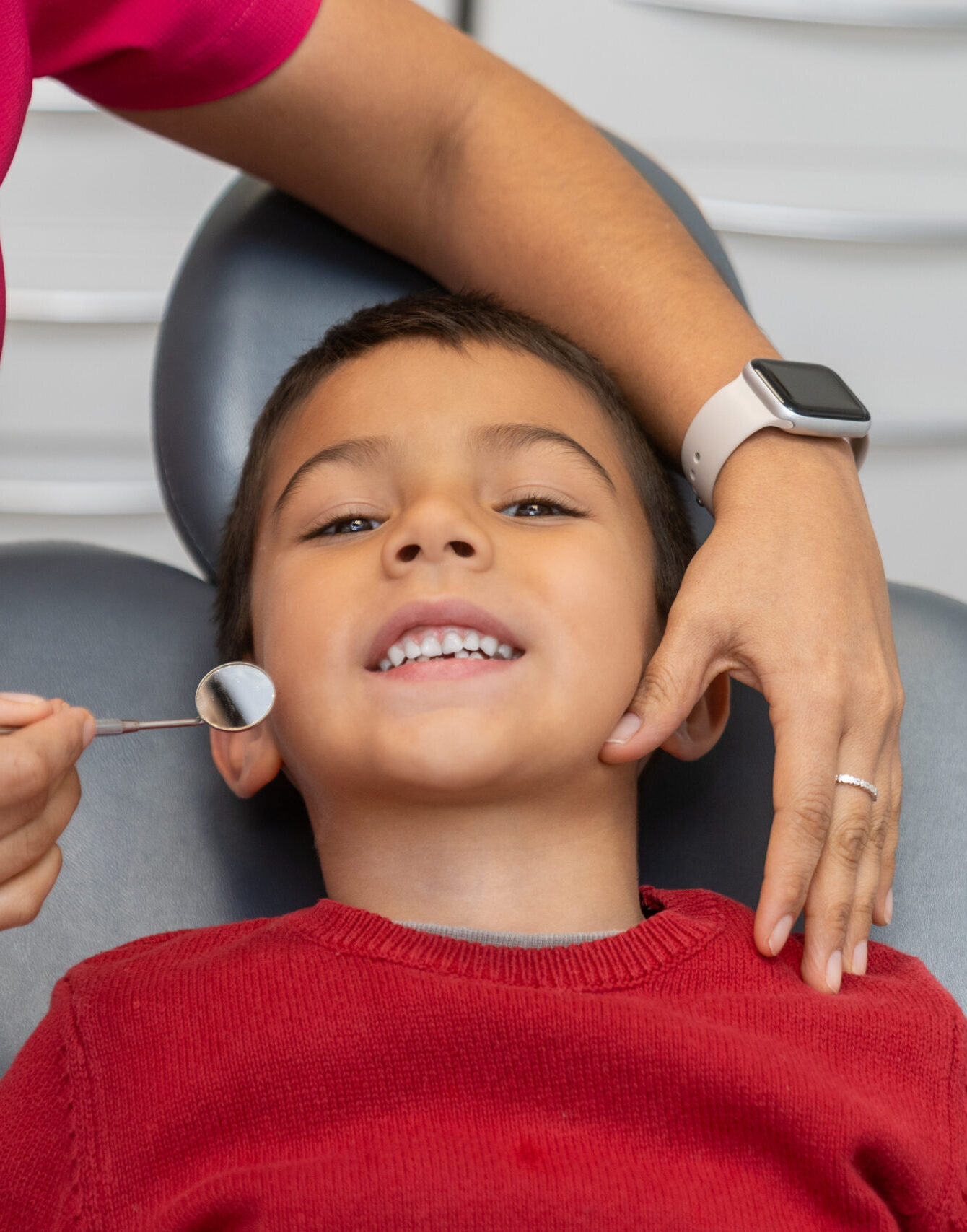 Pediatric dentist using a dental mirror to examine the teeth of a young boy during a routine checkup