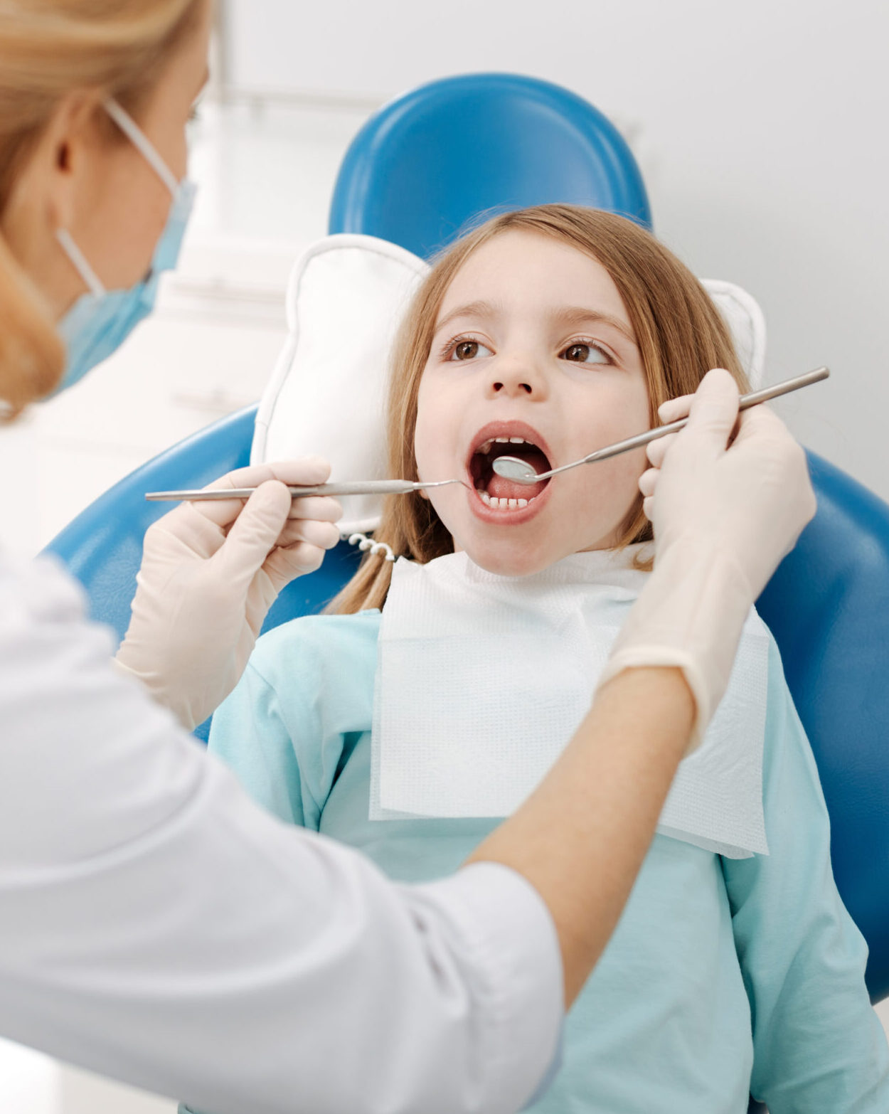 Such a nice lady. Enthusiastic brave little girl sitting in dentists chair and keeping her mouth open while the doctor having a look at her teeth