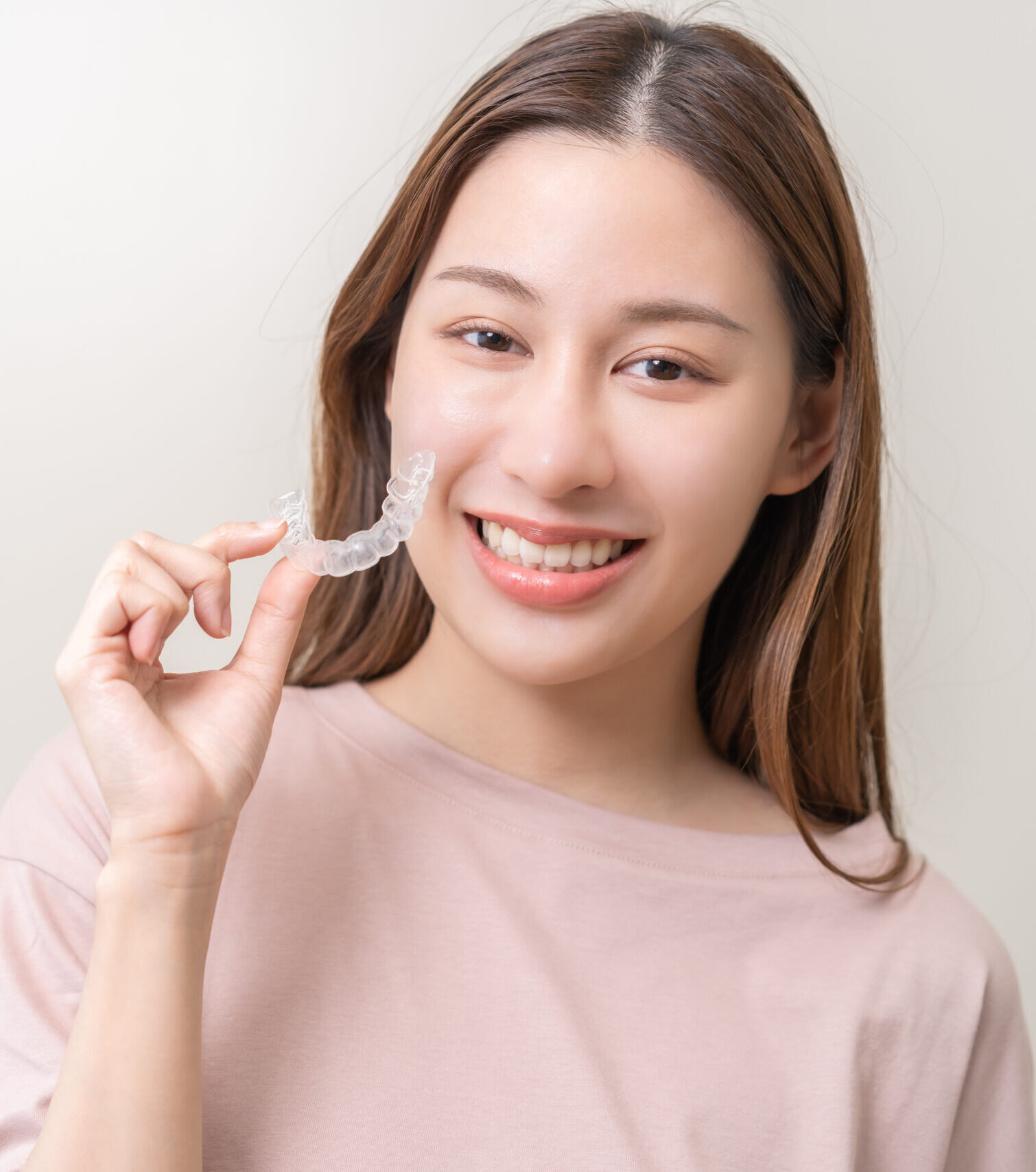 Dental invisible braces, beautiful smiling asian young woman holding invisalign braces, wearing orthodontic silicone trainer, white smile using invisible whitening tray. Stomatology, dental healthcare