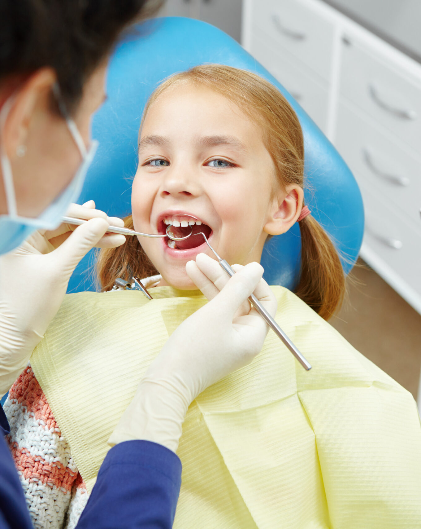 Female dentist examines of smiling child at the pediatric dentistry clinic. Happy little girl