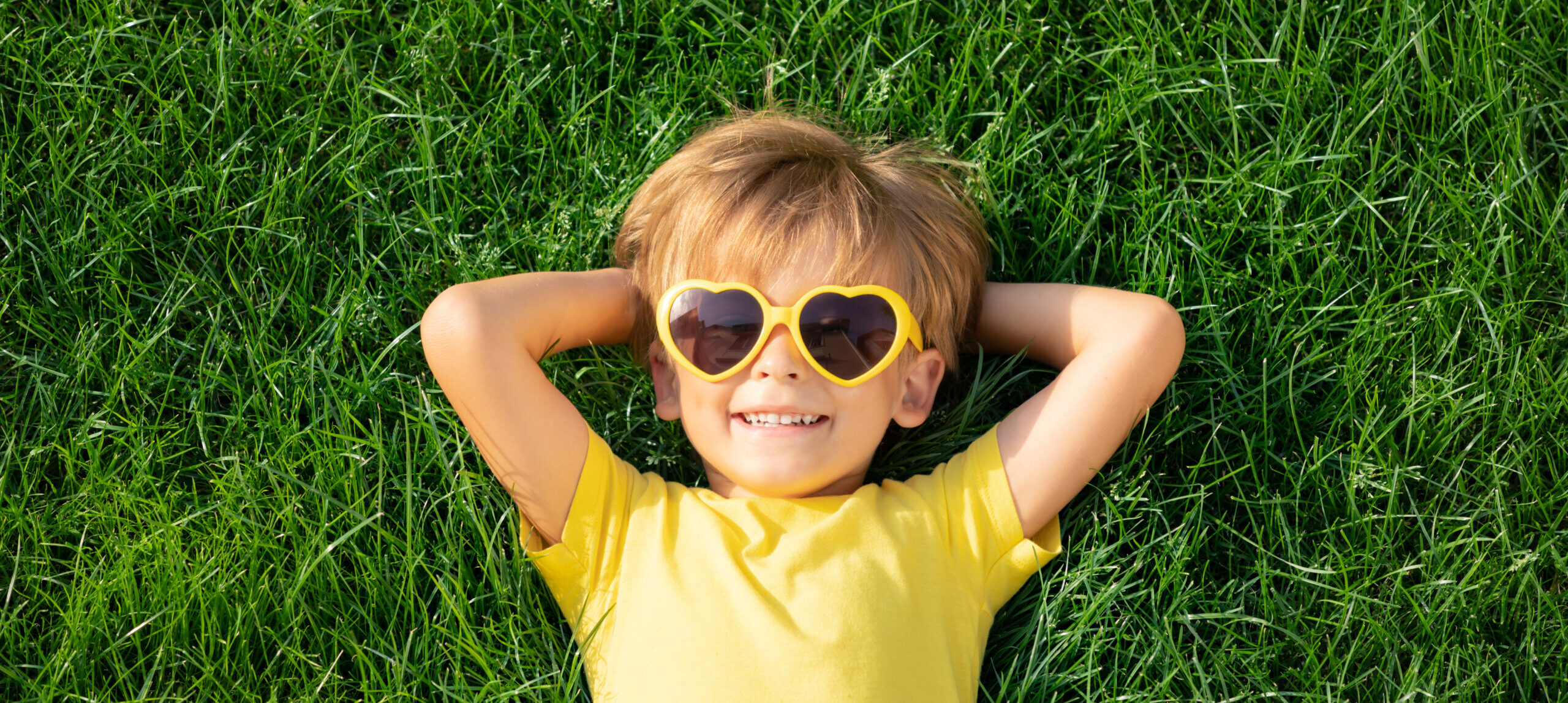 Happy child playing outdoor in spring park. Kid lying on green grass. Earth day and ecology concept. Top view portrait of boy outside