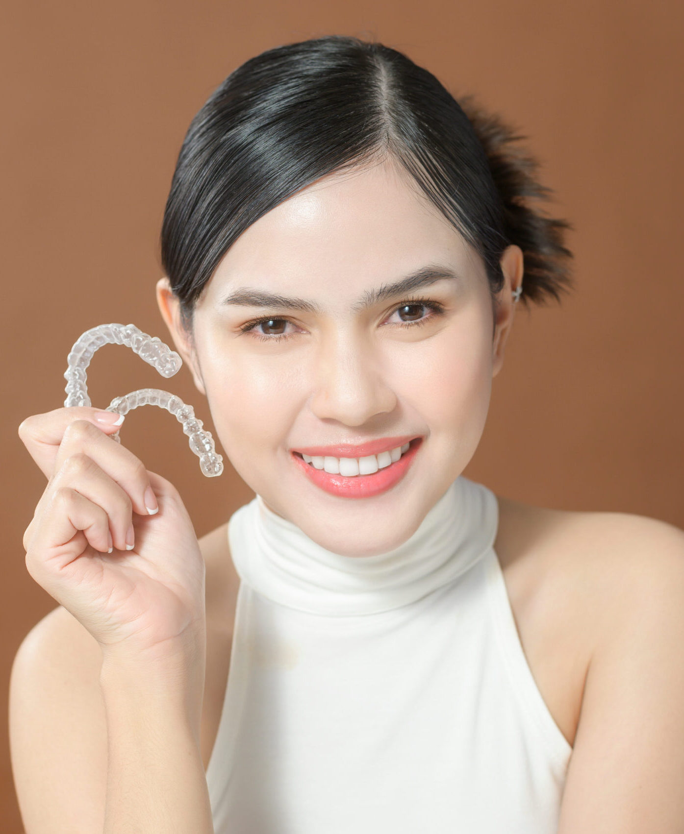 A young woman with beautiful teeth is holding Invisalign, healthy dental concept