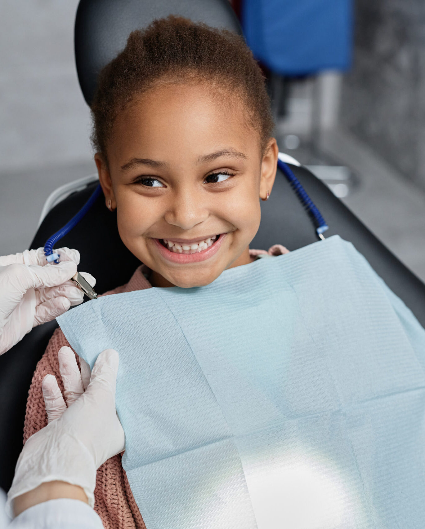 Portrait of smiling little girl in dental chair with nurse preparing her for teeth check up, copy space