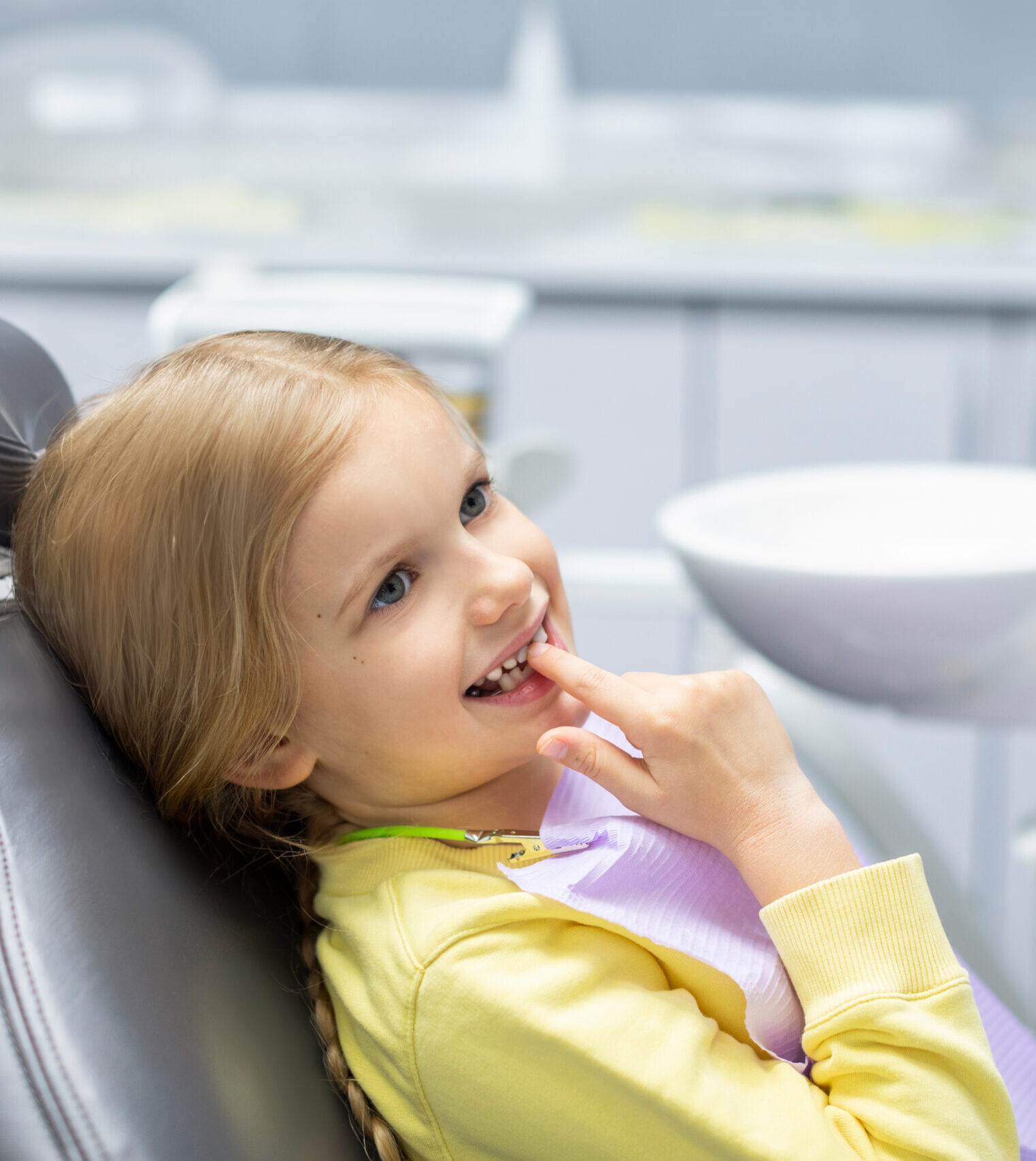 Cute little girl showing her milk teeth and waiting for checkup, sitting in chair in dentist office. Early prevention and no fear concept