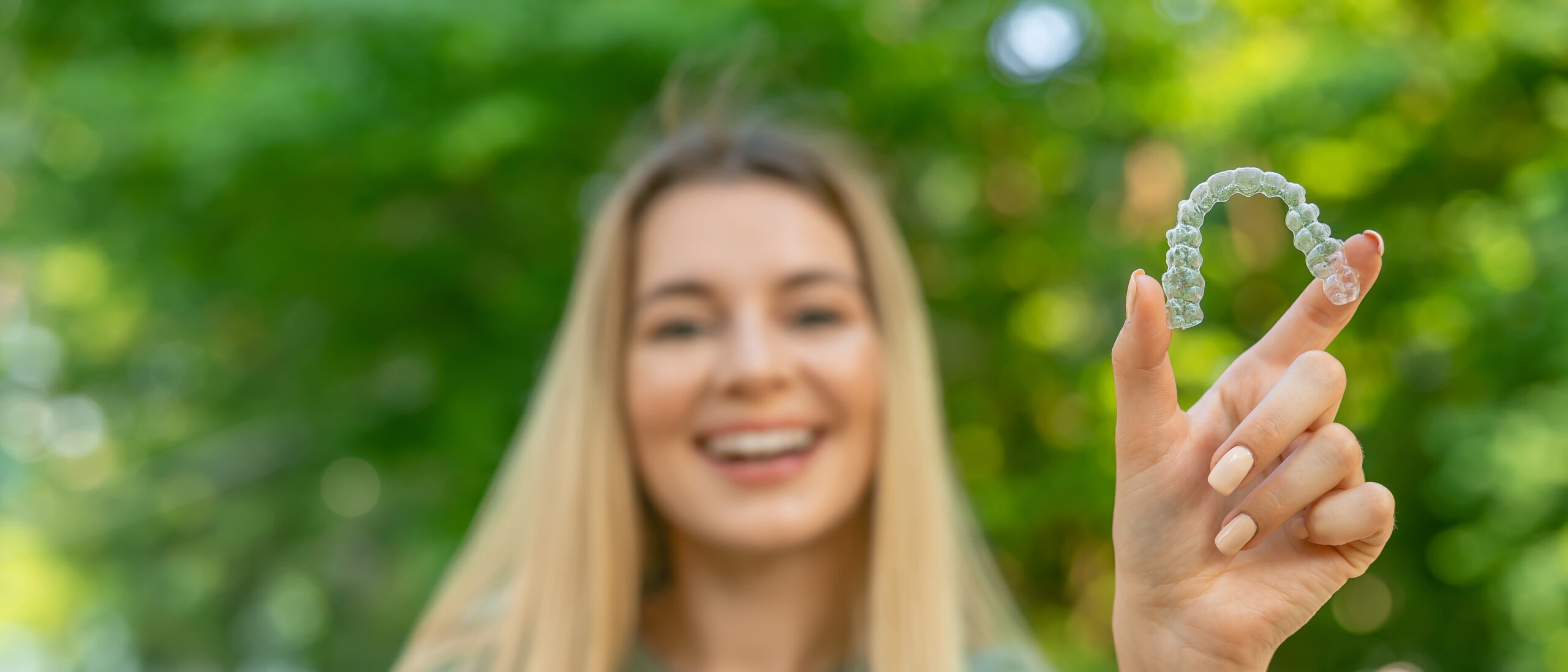 Happy girl in green t-shirt holding removable braces or aligners for straightening and whitening teeth on green background